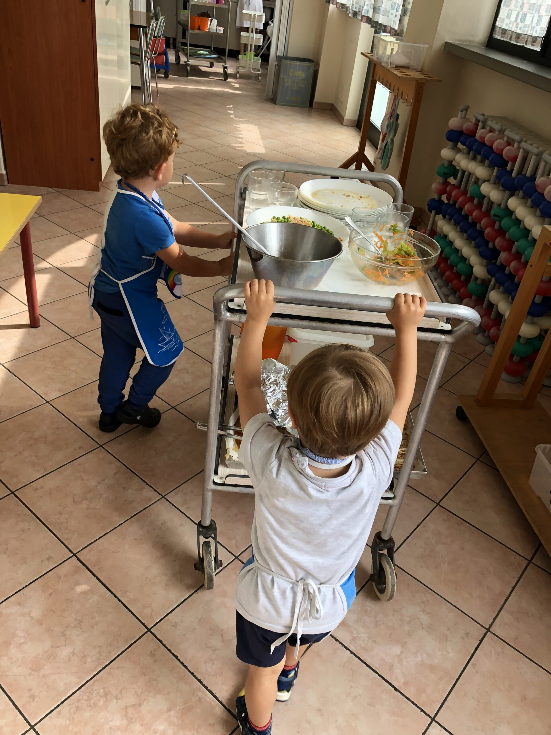 Due bambini sparecchiano la tavola utilizzando un carrello